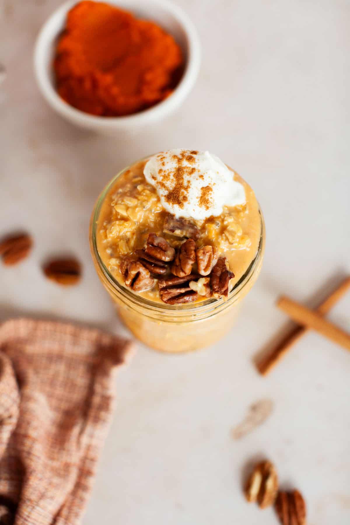 Pumpkin overnight oats in a mason jar topped with pecans, whipped cream and cinnamon.