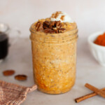 Pumpkin overnight oats in a mason jar topped with pecans and whipped cream.