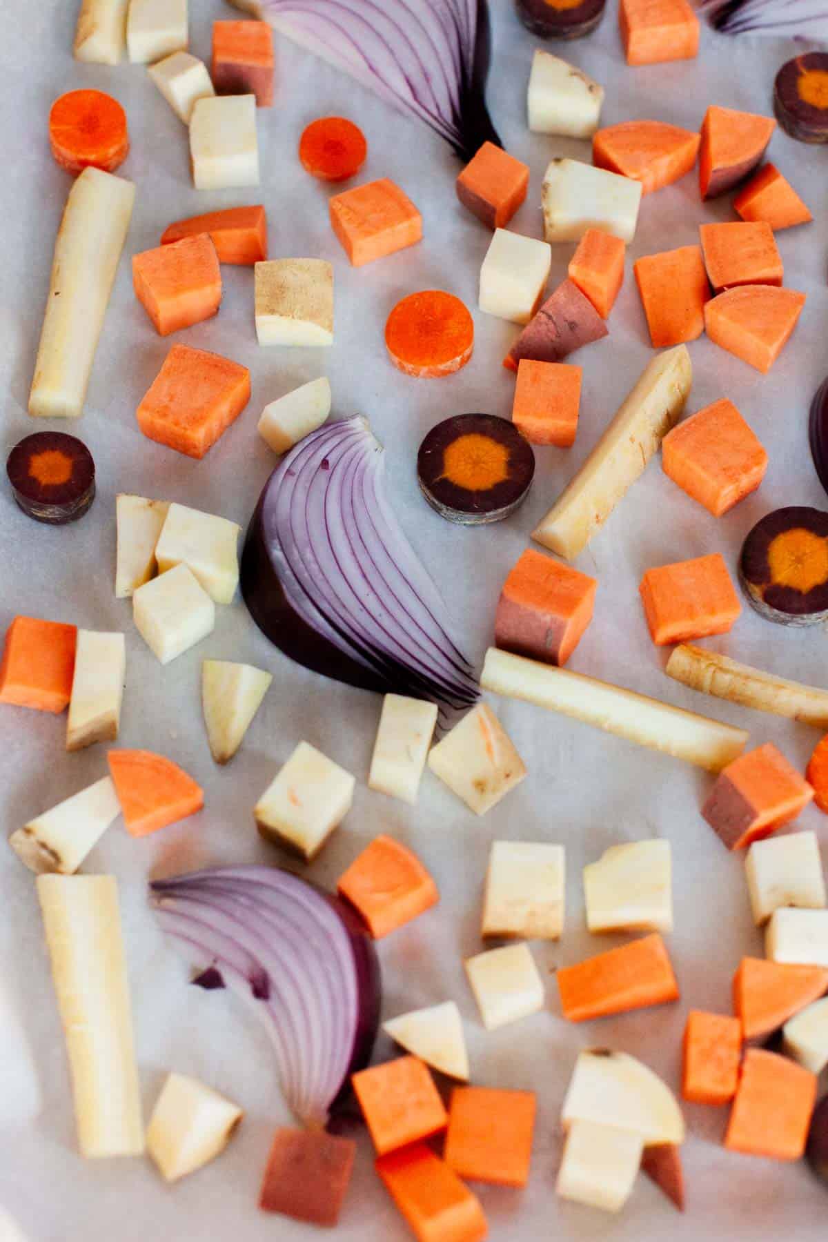 A baking sheet with red onion wedges, carrots, yams and white sweet potatoes.