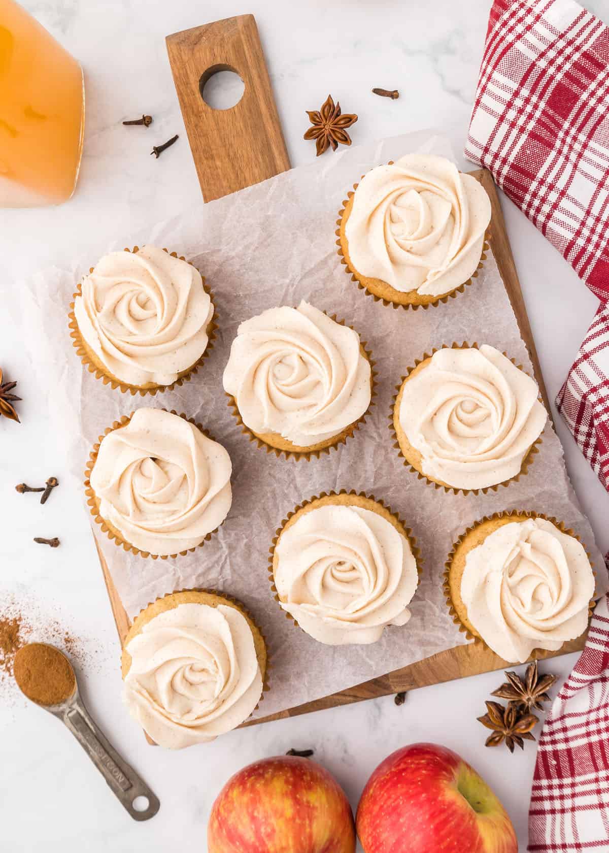 Apple spice cupcakes with cinnamon frosting and apples on a cutting board.