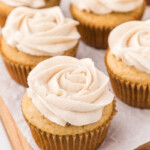 Apple spice cupcakes with cinnamon frosting on a wooden cutting board.