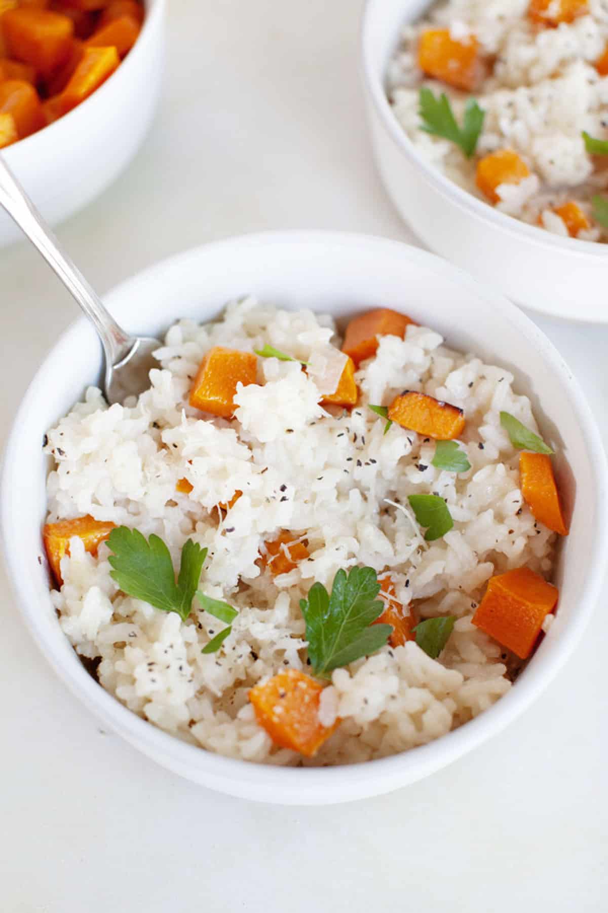 Two bowls of butternut squash risotto with carrots and parsley.