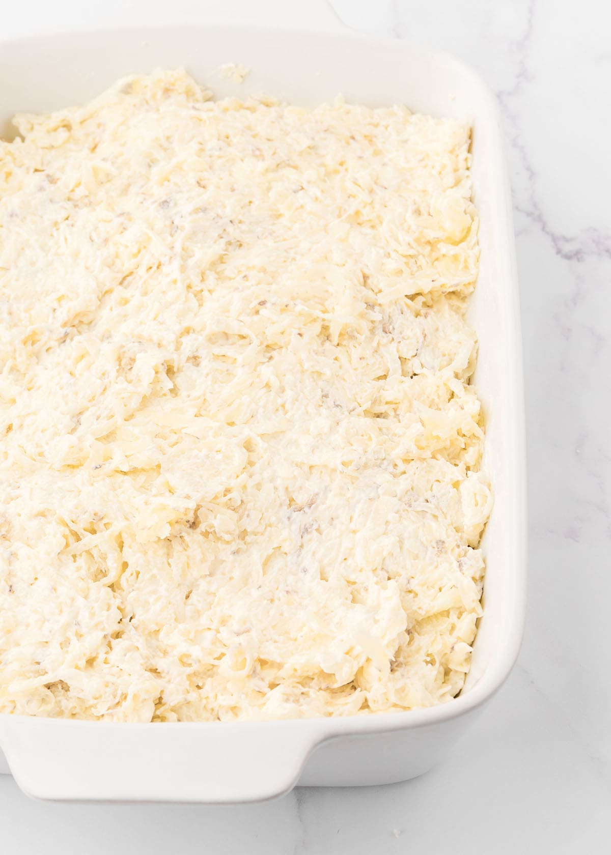 A white baking dish filled with shredded cheese.