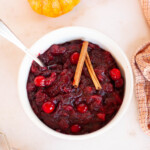 A bowl of cranberry sauce with cinnamon sticks and a spoon.