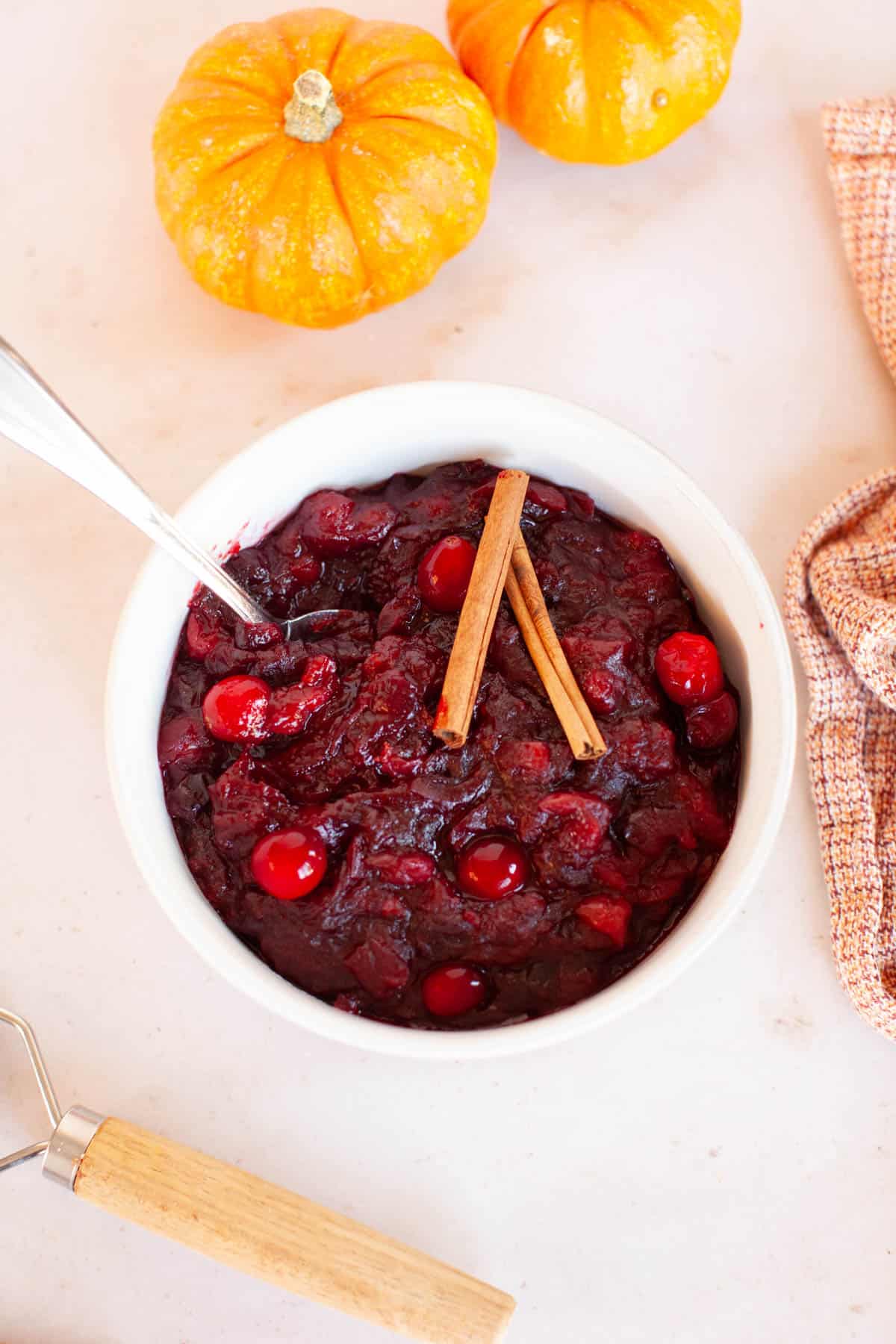 A bowl of cranberry sauce with cinnamon sticks and a spoon.