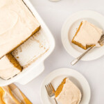 Two slices of pumpkin cake with frosting on white plates with forks.