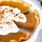 A pumpkin pie with whipped cream and a slice taken out.