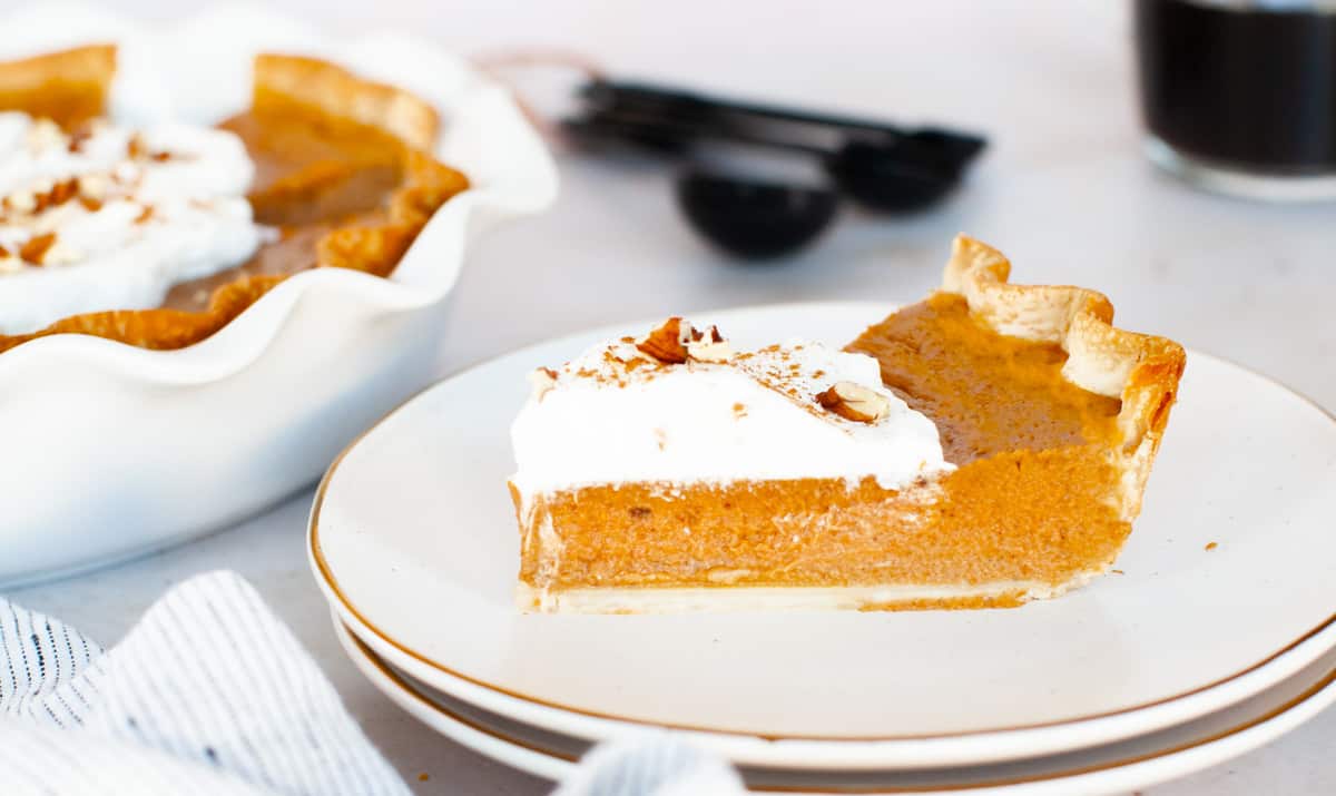 A slice of pumpkin pie with whipped cream on a plate.