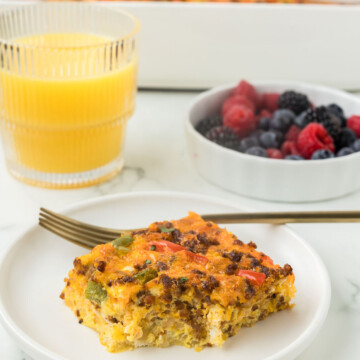 Breakfast casserole on a plate with berries and orange juice.