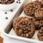Chocolate chip cookies on a baking sheet on a counter with a spoonful of cocoa powder.