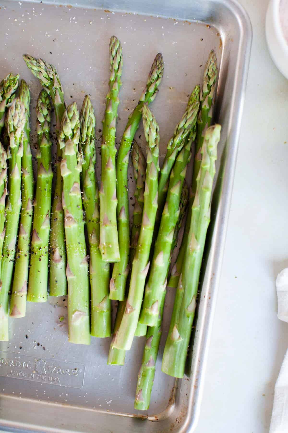 Uncooked asparagus spears on a baking sheet.