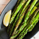 Grilled asparagus on a black plate with a lemon wedge.