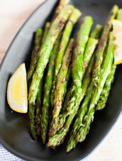 Grilled asparagus on a serving plate with lemon wedges.