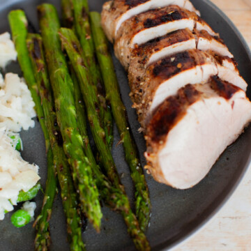 Slices of marinated pork tenderloins with asparagus and risotto on a plate.
