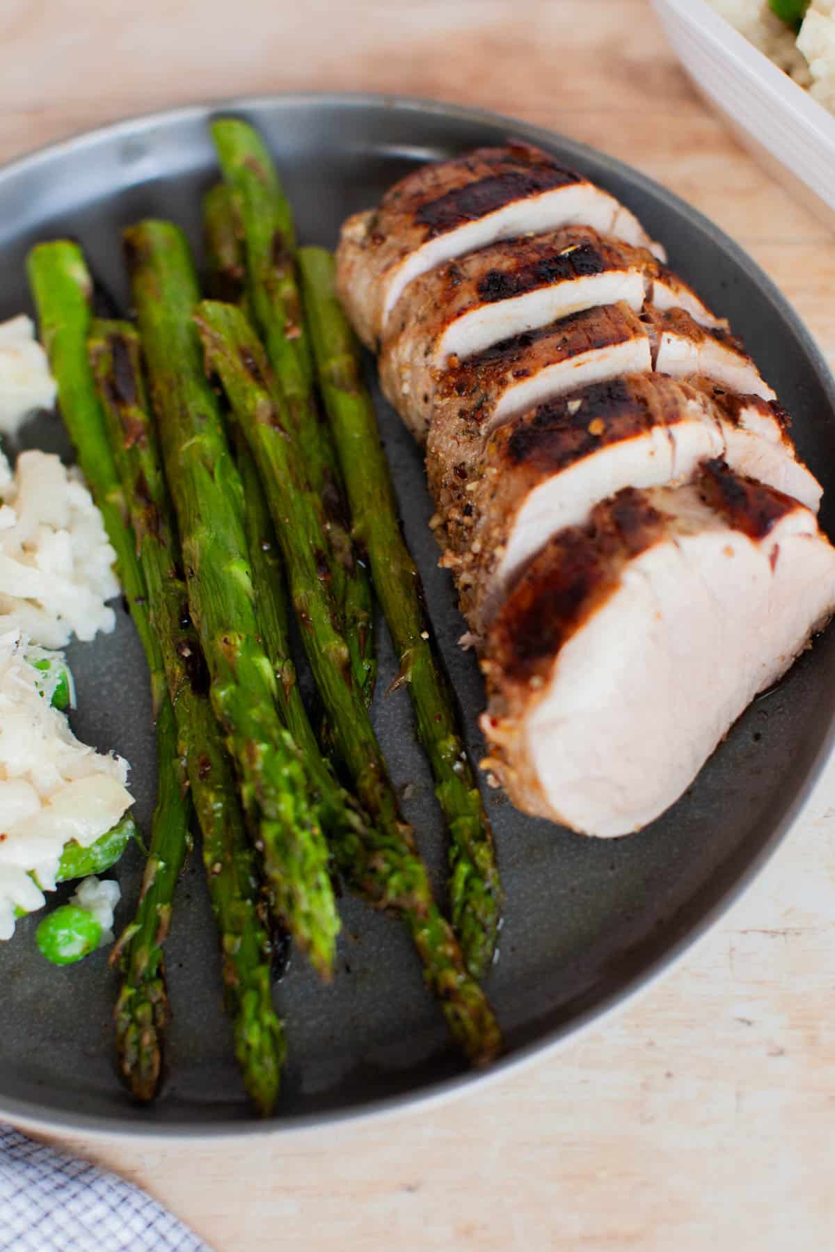 Slices of marinated pork tenderloins with asparagus and risotto on a plate.