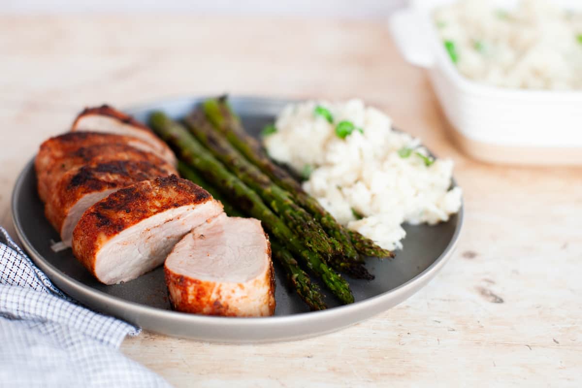 Slices of marinated pork tenderloins with asparagus and risotto on a gray plate.