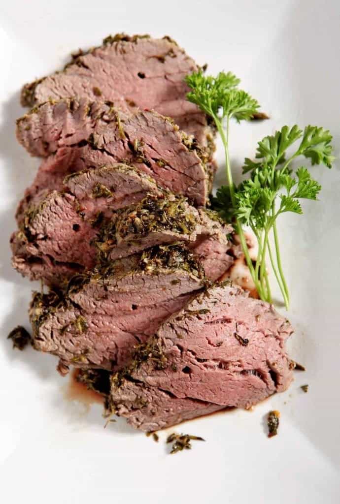 Beef tenderloin with herbs on a white plate.