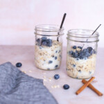 Blueberry overnight oats on a table with a blue cloth napkin and cinnamon sticks.