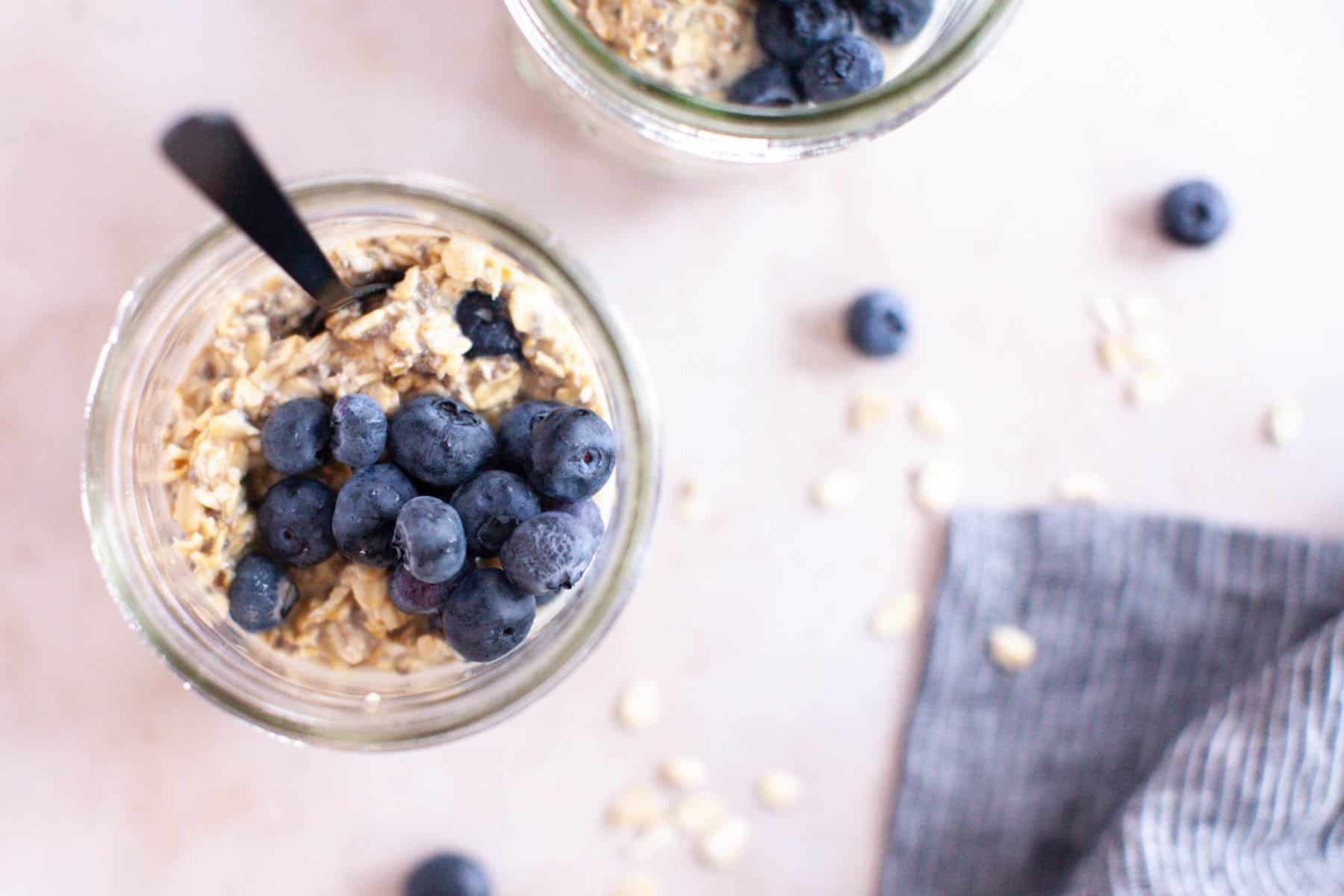 Two jars of blueberry overnight oats with spoons.