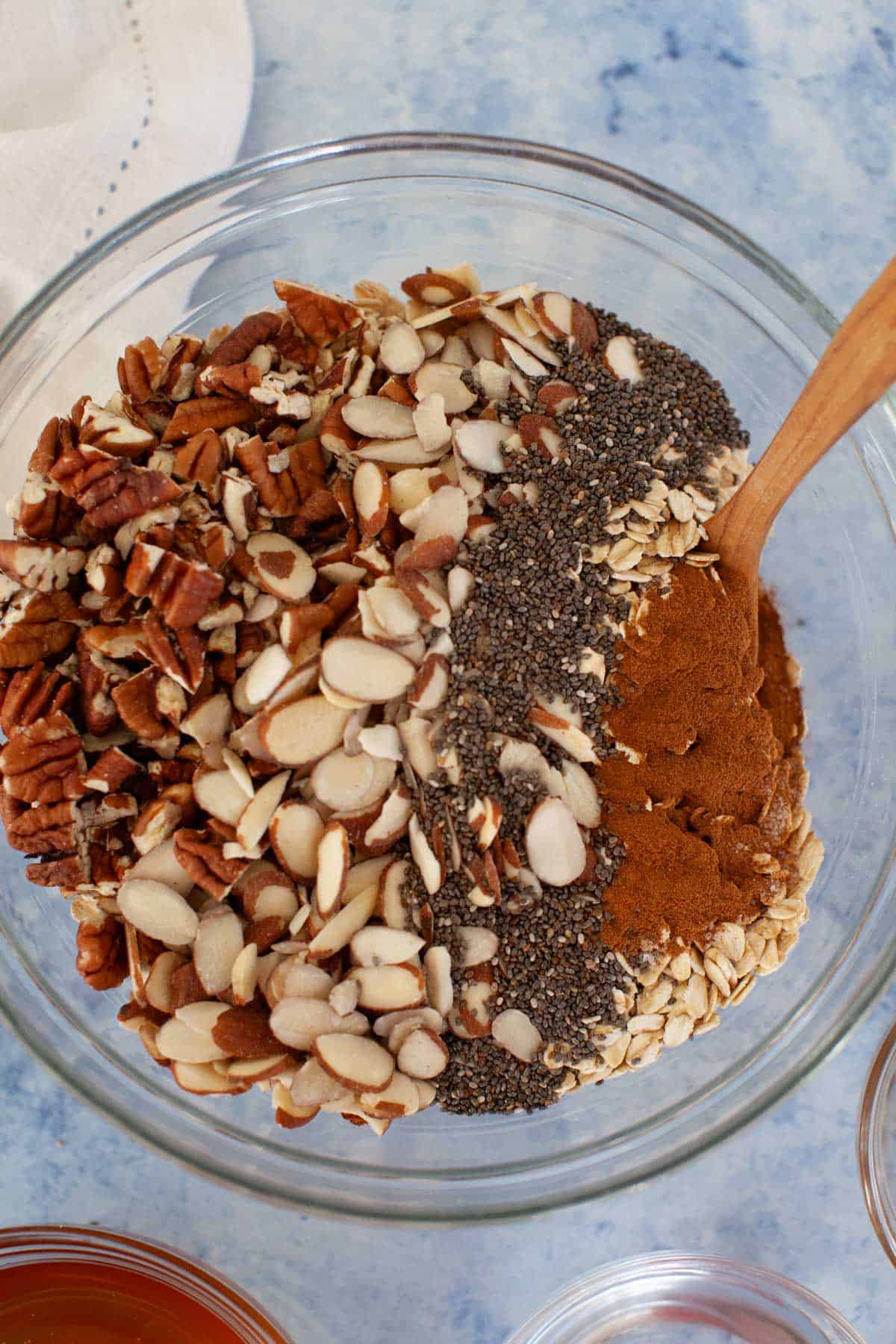 Oats, pecans, sliced almonds, chia seeds, and cinnamon in a glass bowl.