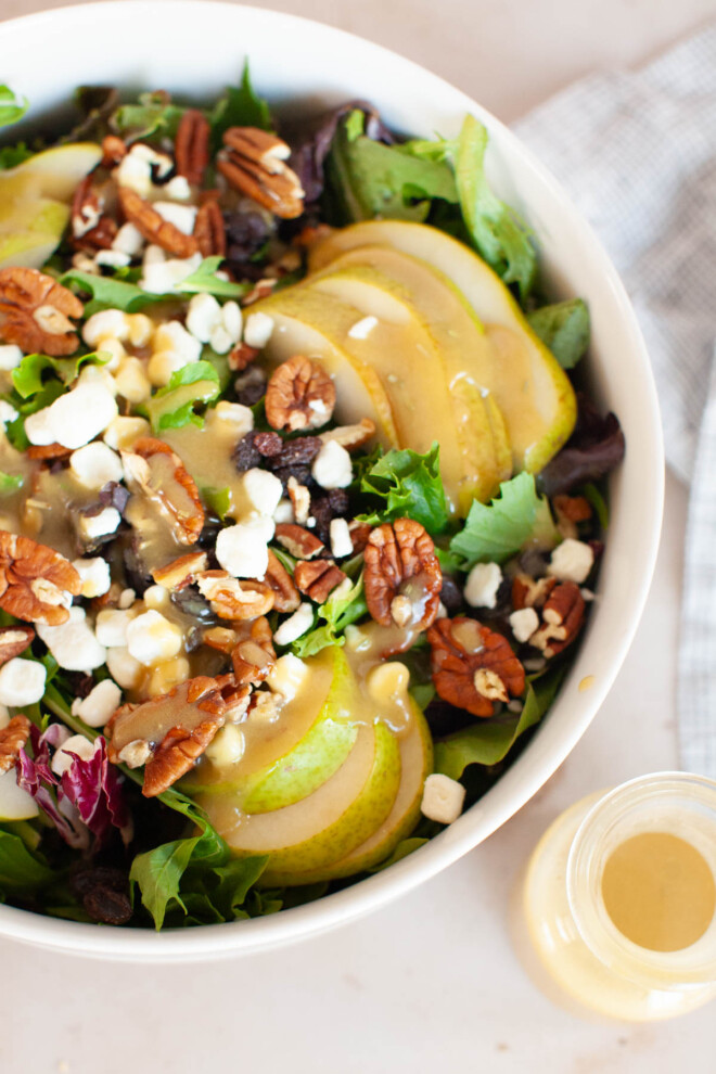 A white bowl with pear salad, goat cheese, raisins and pecans.