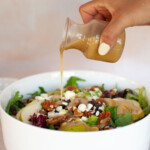 A person pouring a dressing over the pear salad in a white bowl.