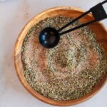 Herbs and spices mixed together on a wooden plate with a measuring spoon.