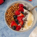 Yogurt bowl on a blue countertop with granola, berries, chia seeds, and honey.