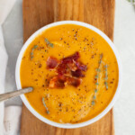 Butternut squash soup topped with bacon and thyme on a wooden serving platter.