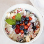 A bowl of creamy fruit salad with mixed berries and mint.