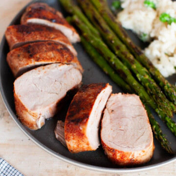 A plate with sliced pork, asparagus and risotto.