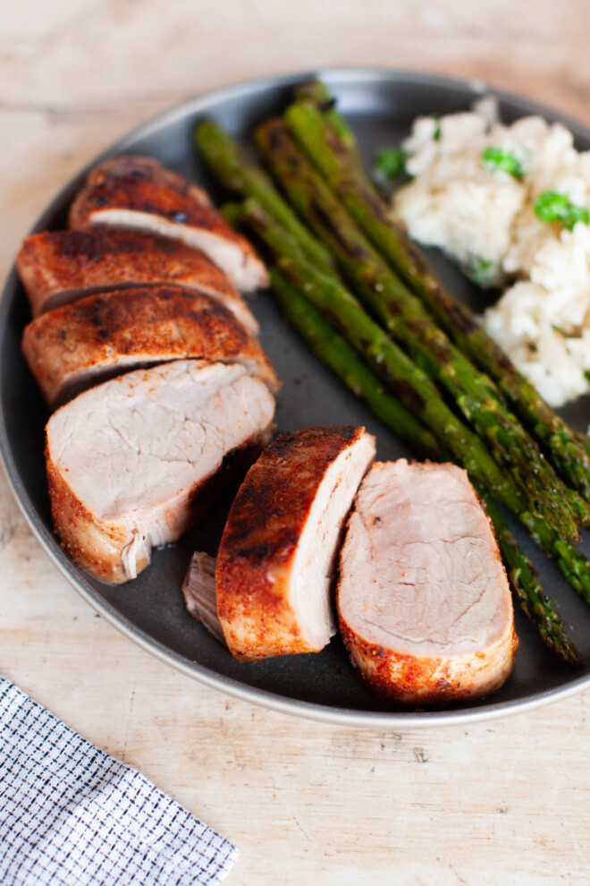 A plate with sliced pork, asparagus and risotto.