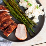 A plate with slices of dry rub pork tenderloin, risotto and asparagus on it.