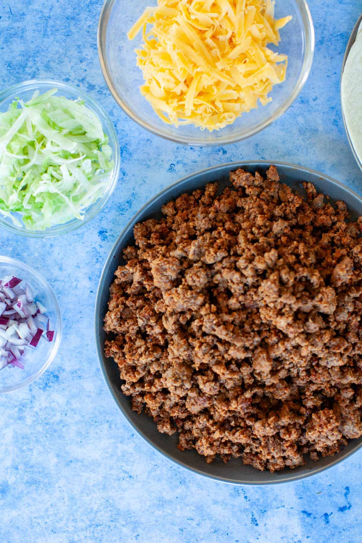 Ingredients for ground beef tacos on a blue countertop.