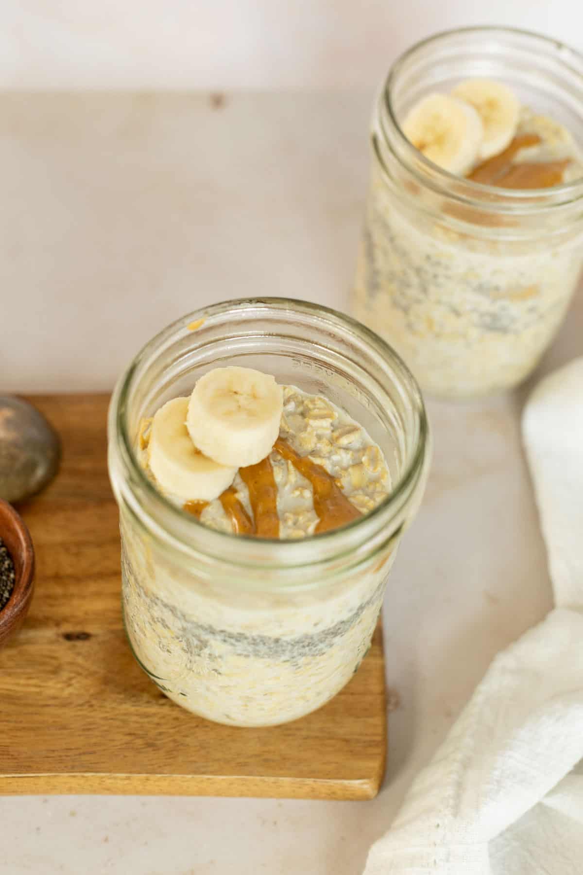 Jars of peanut butter overnight oats with chia seeds on a cutting board.