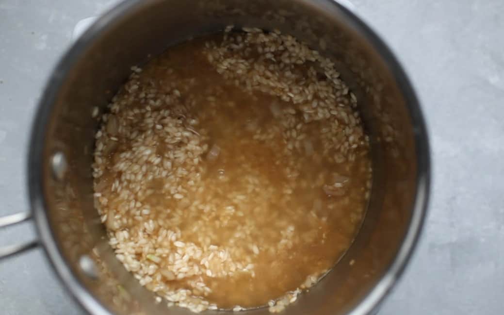 A pot filled with chicken brother, risotto rice and a wooden spoon.