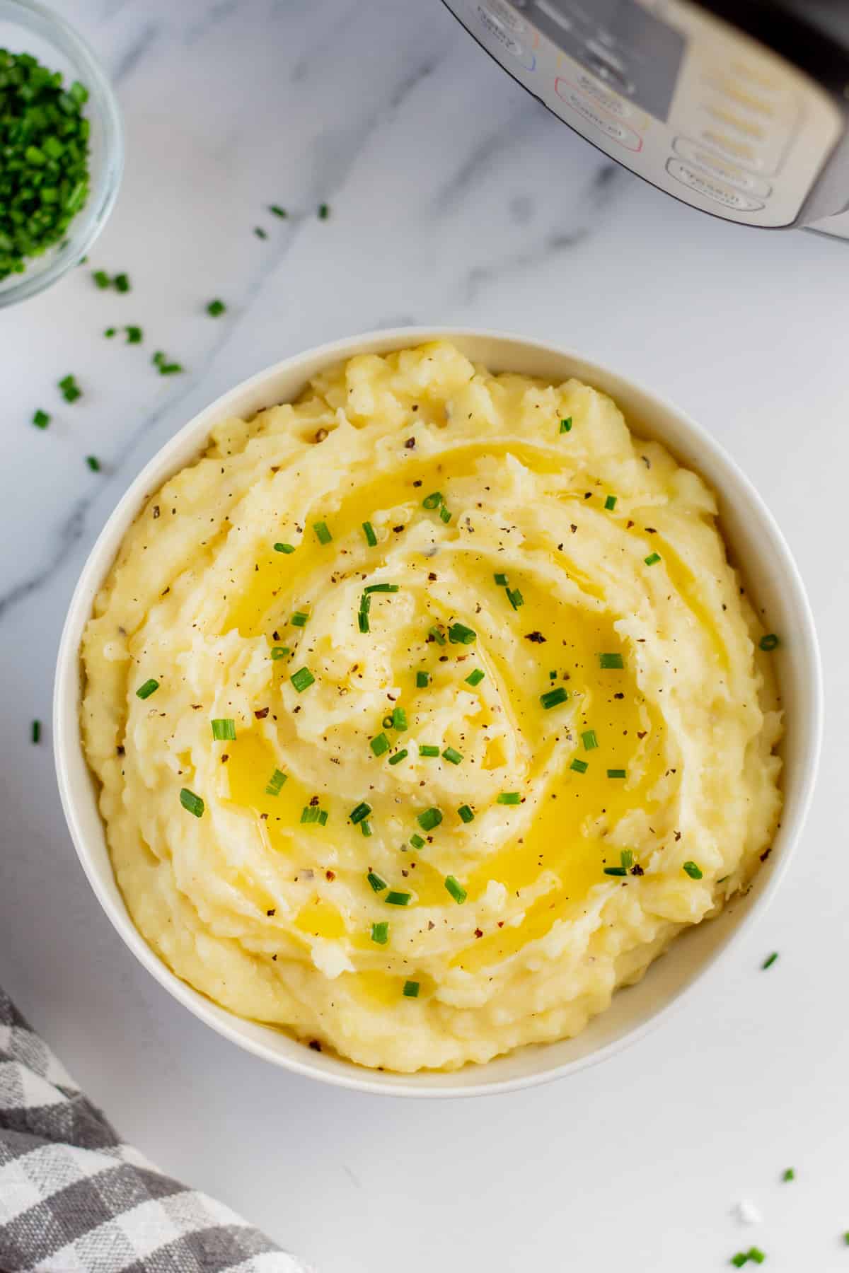 A bowl of instant pot mashed potatoes garnished with melted butter and chopped chives.