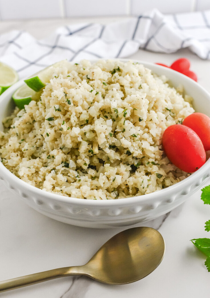 Cilantro cauliflower lime rice in a bowl with cherry tomatoes served on a kitchen counter.