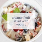 Bowl of creamy fruit salad with yogurt garnished with fresh mint.