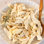 Shredded chicken breast with herbs in a bowl with a wooden spoon.