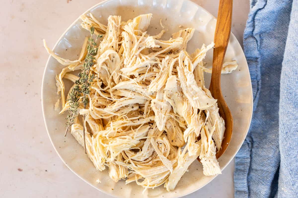 Plate of shredded chicken with herbs on a kitchen counter.
