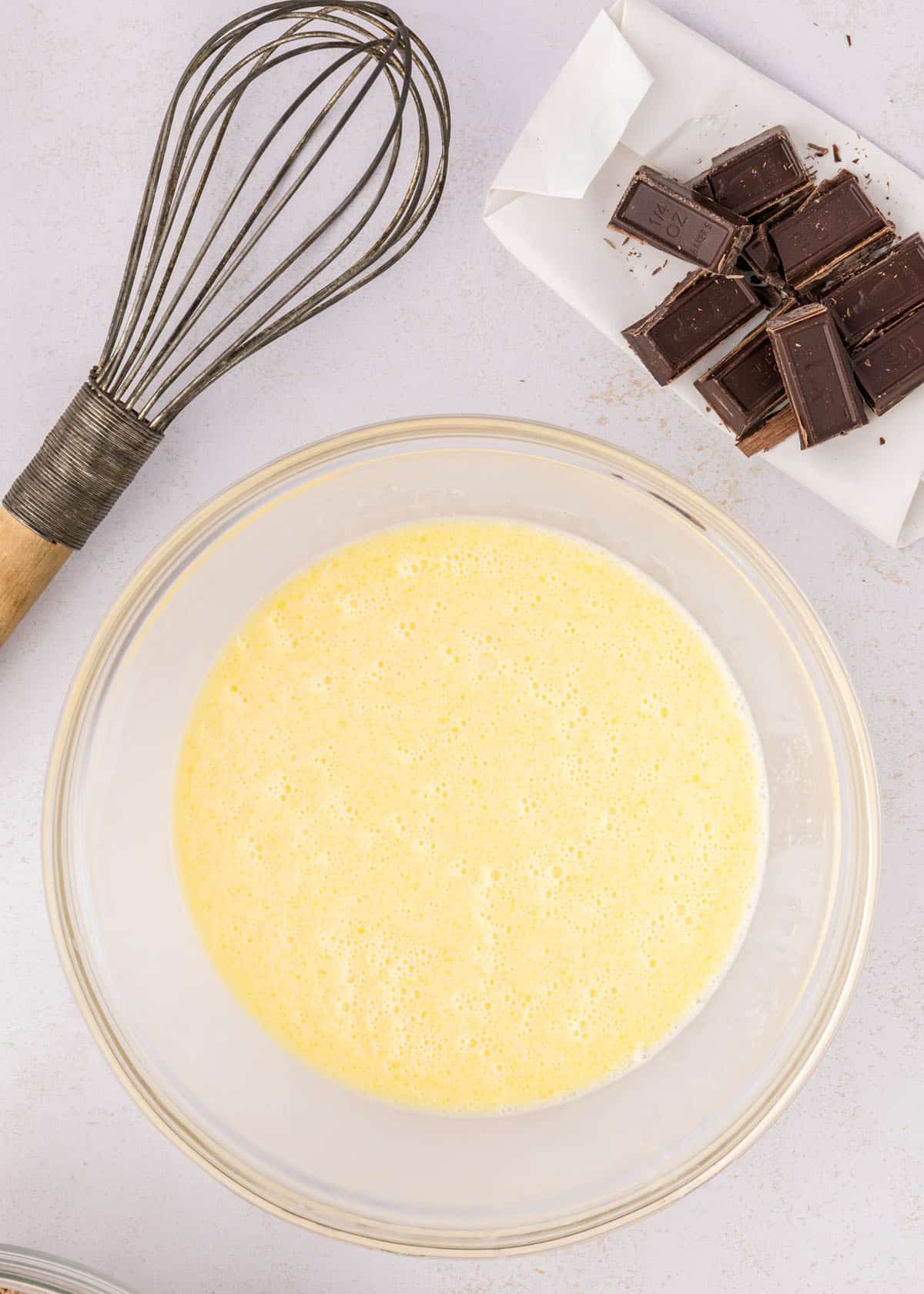 Bowl of whipped batter with a whisk and chopped chocolate on the side.