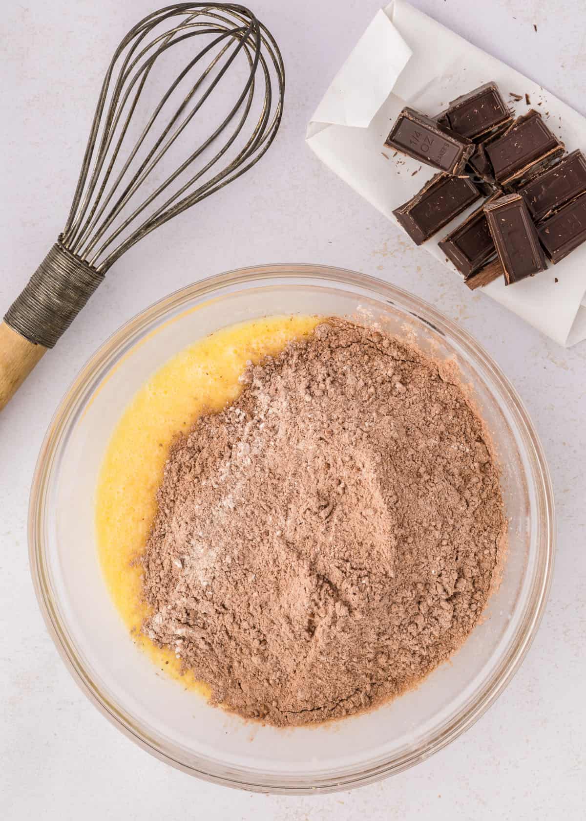Ingredients for chocolate pancakes preparation with a whisk and chocolate pieces on a kitchen counter.