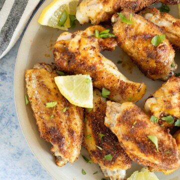 A plate of dry rub chicken wings garnished with lime wedges and chopped parsley, served on a light-colored plate.