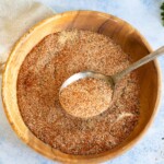 A chicken wing dry rub being scooped out of a wooden bowl with a spoon.