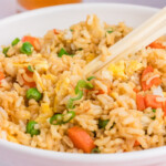 Bowl of fried rice with peas, carrots, and egg, garnished with green onions and served with chopsticks.