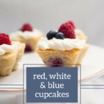 A plate with cupcakes topped with white frosting and decorated with red raspberries and blue blueberries. Text on the image reads "Red White and Blue Cupcakes" and "joyfullymad.com".