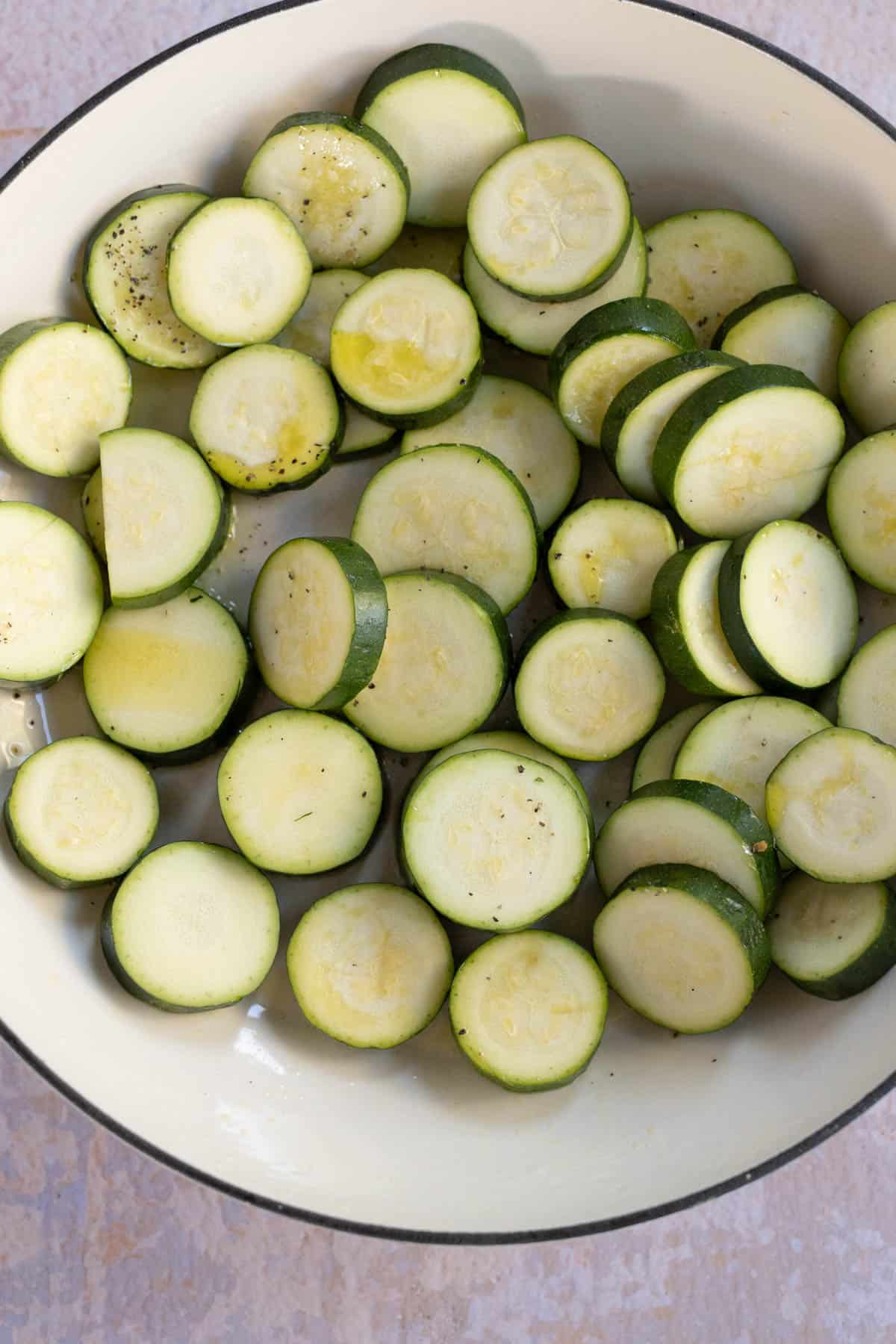 A bowl filled with sliced and seasoned raw zucchini.