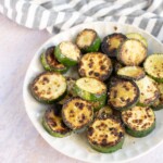 A plate of sauteéd zucchini slices placed beside a gray and white striped cloth on a light-colored surface.