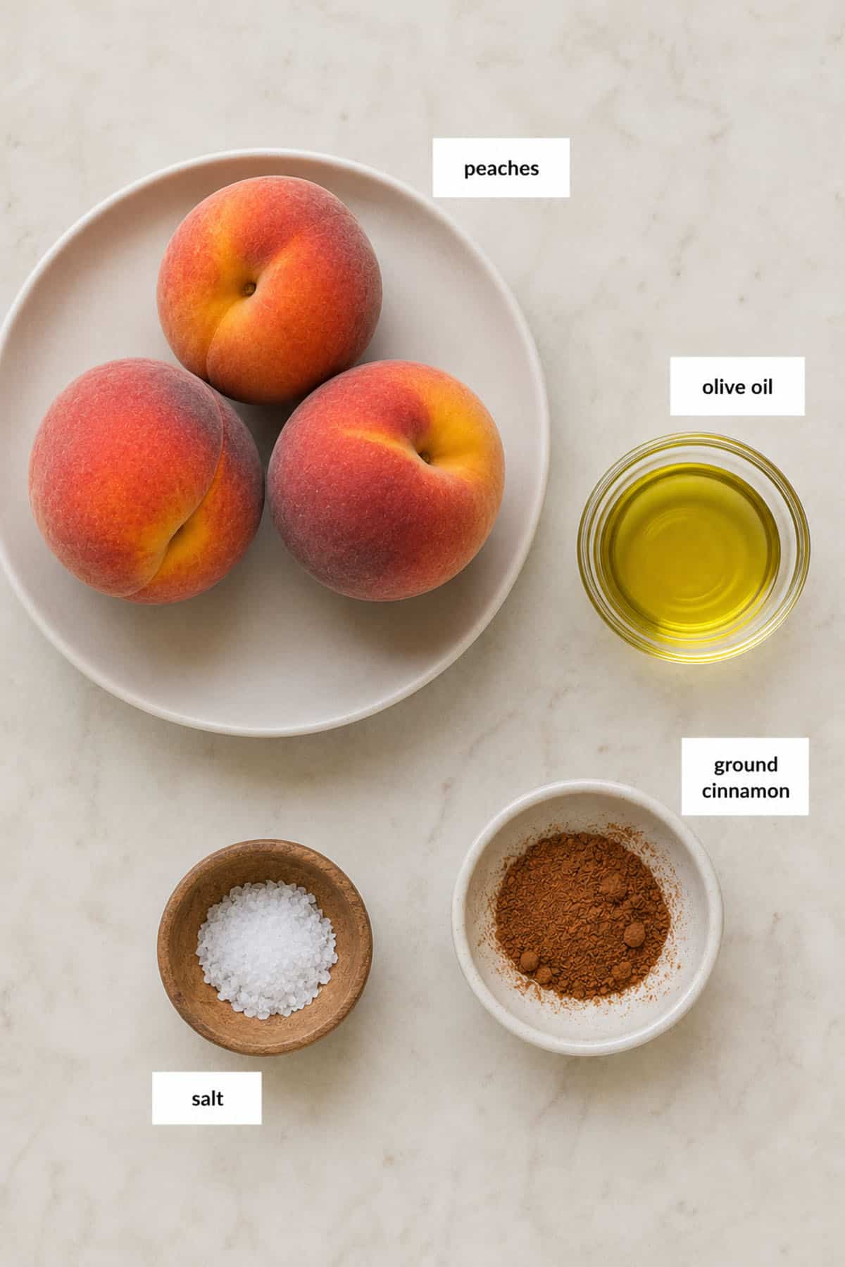 Three peaches on a plate, with small bowls of olive oil, ground cinnamon, and salt arranged on a light surface. Each item is labeled.
